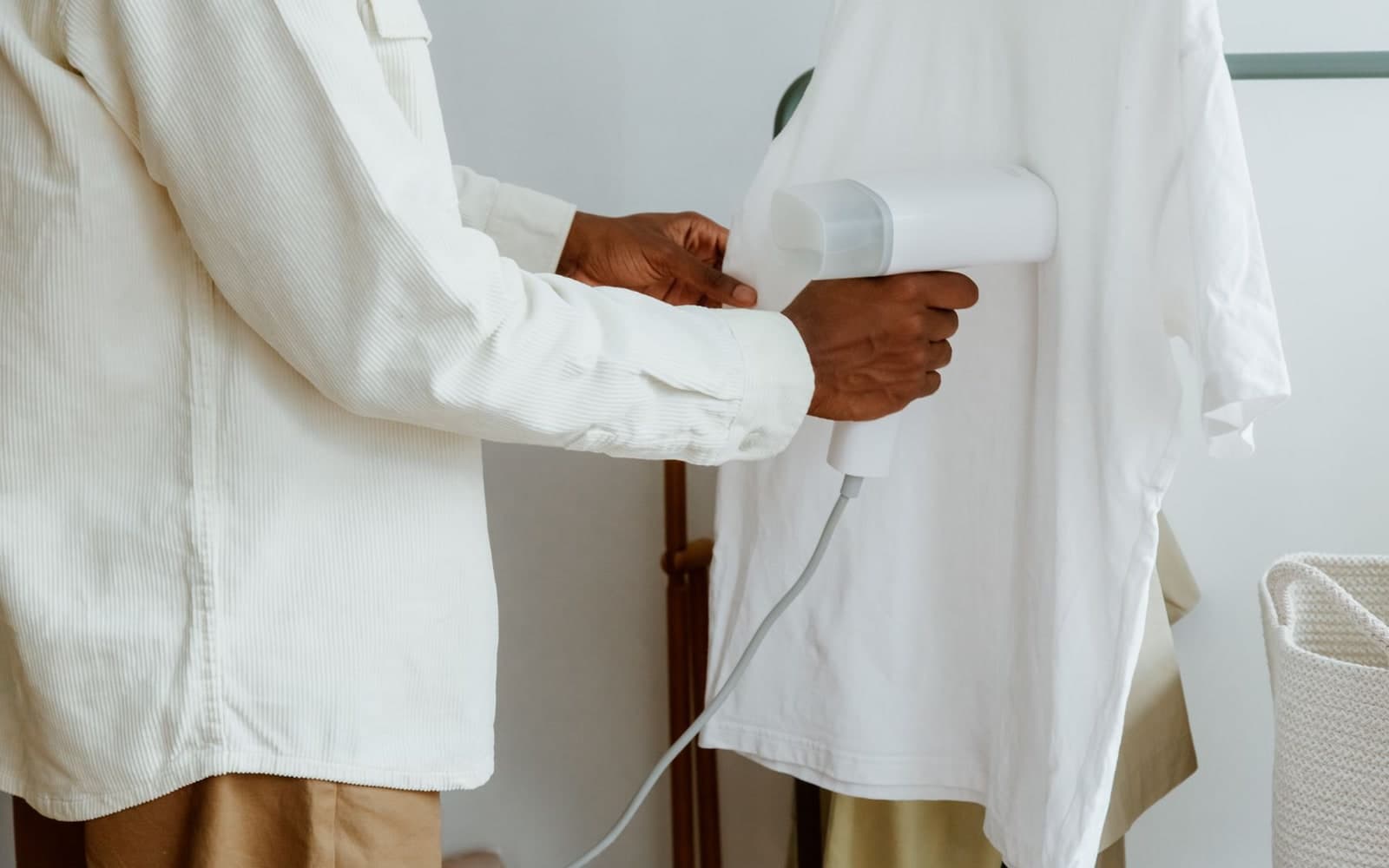Man using a garment steamer on a white shirt hanging from a clothing rack