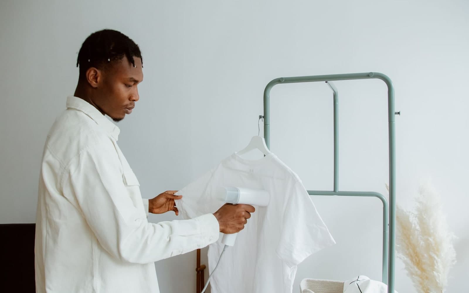 Man freshening a white shirt on a clothing rack with a handheld steamer