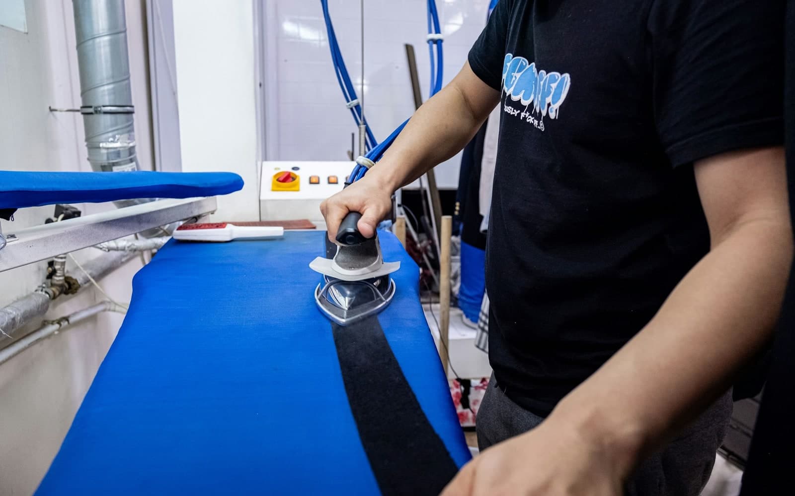 Worker operating finishing equipment on a padded board in a dry cleaning workroom