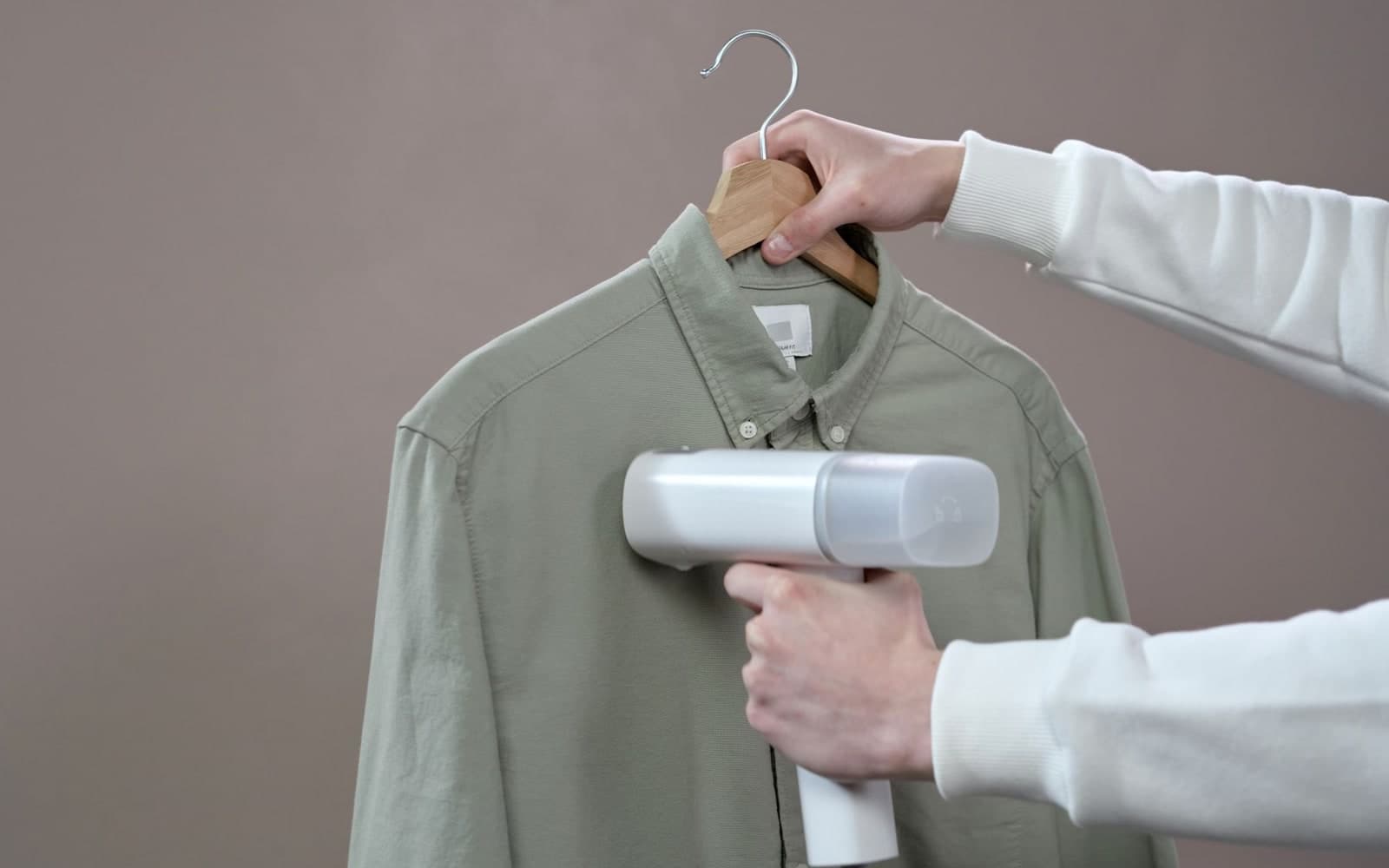 Hands steaming a green shirt with a portable garment steamer