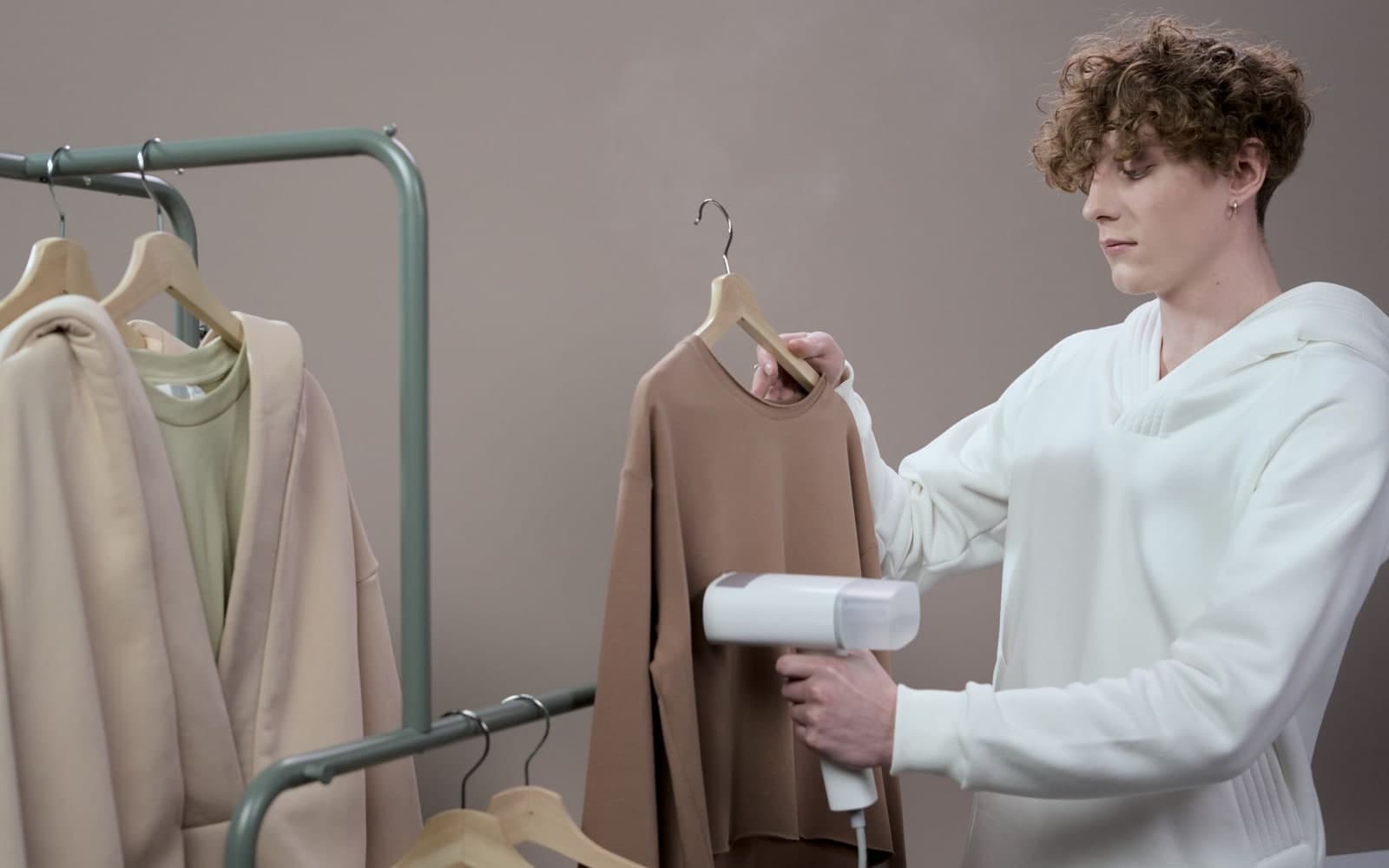 Young man steaming a sweatshirt on a rail in a clothing studio
