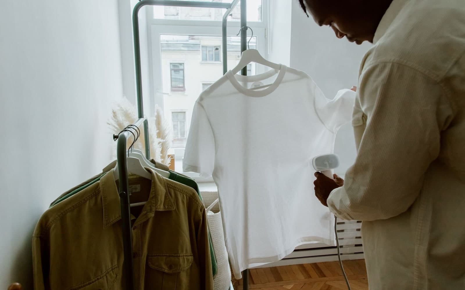 Man running a steamer down a white shirt hanging from a clothing rack