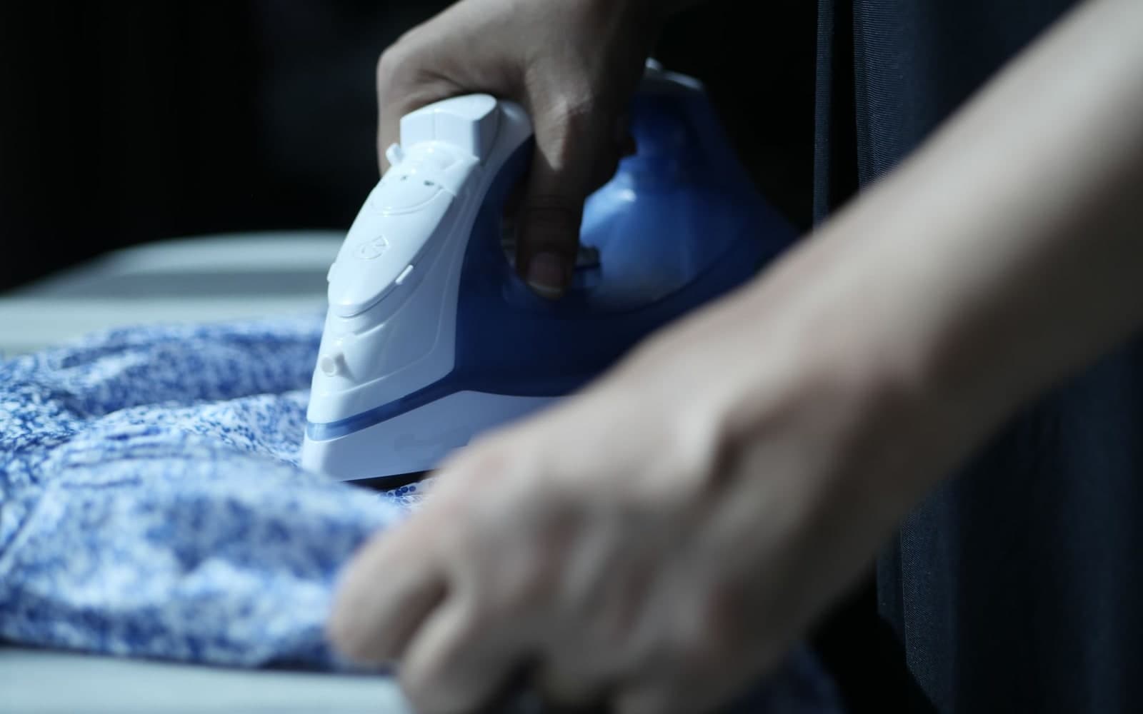 Hands guiding a steam iron over blue fabric on an ironing board